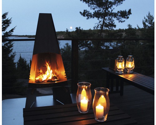 Atmosphärische Gartenszene mit Kaminofen, Windlichtern und Laternen auf einer Holzterrasse am See.