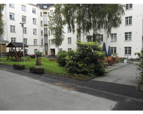 Cour intérieure avec balançoire, parterres de fleurs, arbres et sièges devant un immeuble de plusieurs étages.