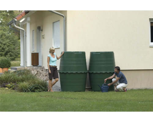 Zwei grüne Regentonnen im Garten vor einem Haus, ein Mann befüllt eine Gießkanne