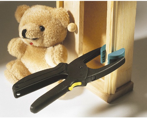 Serre à ressort fixant une pièce de bois sur une armoire miniature, avec un ours en peluche en arrière-plan