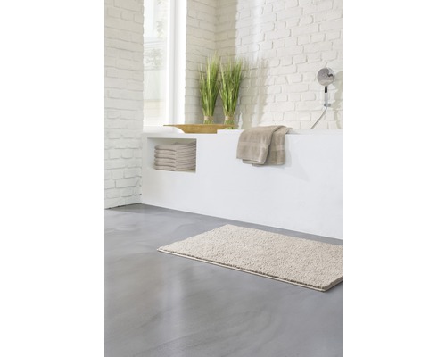 Helles Badezimmer mit Badematte, Handtüchern und Dekoration auf einer gemauerten Badewanne.