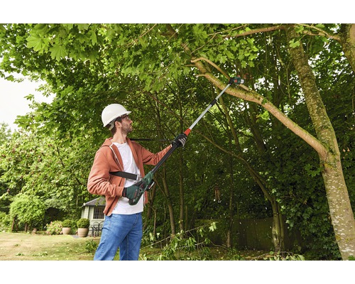 Un homme avec un casque de protection coupe des branches avec une élagueuse sur perche dans le jardin.
