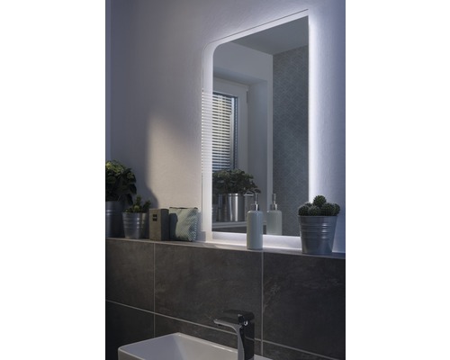 Beleuchteter Badezimmerspiegel über einem Waschbecken mit Armatur und Ablagefläche mit Dekoration