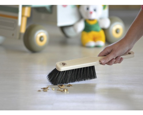 Handfeger mit Holzgriff und dunklen Borsten kehrt Krümel vom Boden.