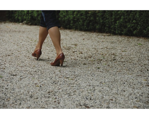 Frau geht auf einem Kiesweg mit Schuhen