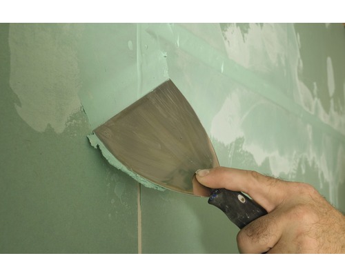 Artisan enduisant une plaque de plâtre avec un couteau à enduire