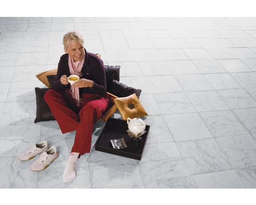 Frau sitzt mit Tasse Tee auf dem gefliesten Boden