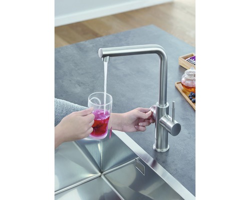 Küchenszene mit Spültischarmatur und Person, die einen Becher mit Tee befüllt