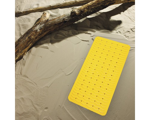 Gelbe Badewannenmatte mit Saugnäpfen auf beigem Untergrund und Holzstamm