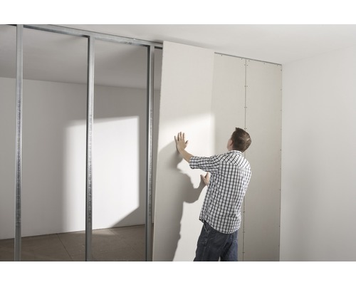 Mann montiert eine Gipskartonplatte an einer Metallunterkonstruktion im Innenbereich