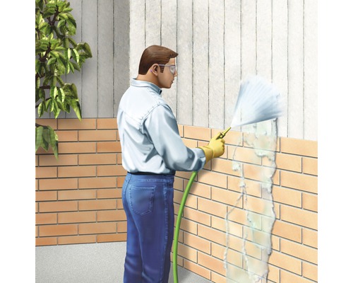 Une personne nettoie un mur en briques avec un nettoyeur haute pression.