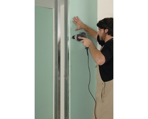 Ein Mann befestigt eine Gipskartonplatte mit einem Akkuschrauber an einer Metallunterkonstruktion.