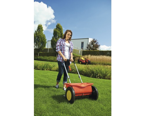 Frau benutzt einen Düngerstreuer im Garten für die Rasenpflege