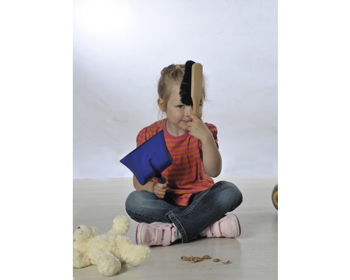 Une fille est assise par terre et joue avec une pelle et une balayette.