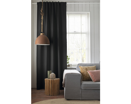 Salon avec canapé, table d''appoint en bois, lampe et rideau noir.