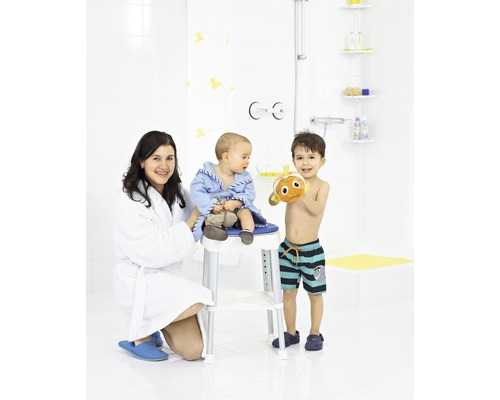 Scène de salle de bains avec une mère, un enfant sur un tabouret de douche et un enfant plus âgé avec un jouet de bain.