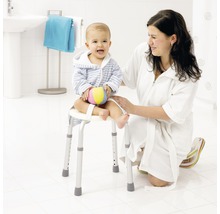 Une femme est agenouillée à côté d''un enfant assis sur un tabouret de douche avec accoudoirs dans une salle de bain lumineuse.