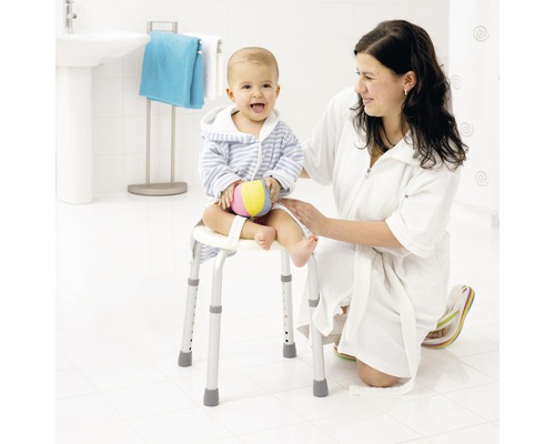 Une femme est agenouillée à côté d''un enfant assis sur un tabouret de douche avec accoudoirs dans une salle de bain lumineuse.