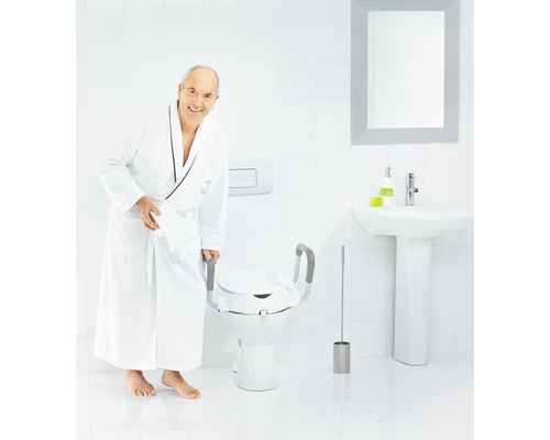 Un homme en peignoir se tient à côté de toilettes avec un rehausseur de siège de toilettes, y compris des barres d''appui.