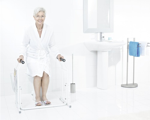 Helles Badezimmer mit Toilette, Waschbecken und einer älteren Frau, die eine Toilettenhilfe benutzt