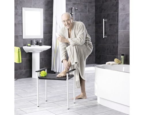 Salle de bains avec baignoire, lavabo et une personne assise sur un tabouret de douche
