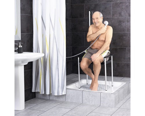 Salle de bains avec rideau de douche, lavabo et homme assis sur un tabouret de douche dans une douche utilisant une douchette