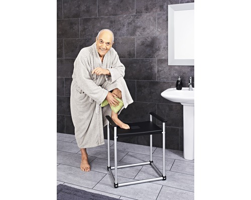 Mann trocknet sein Bein auf einer Duschbank im Badezimmer ab