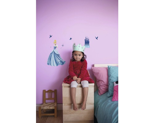 Fille avec une couronne assise devant un mur avec un sticker mural Cendrillon dans une chambre d''enfant