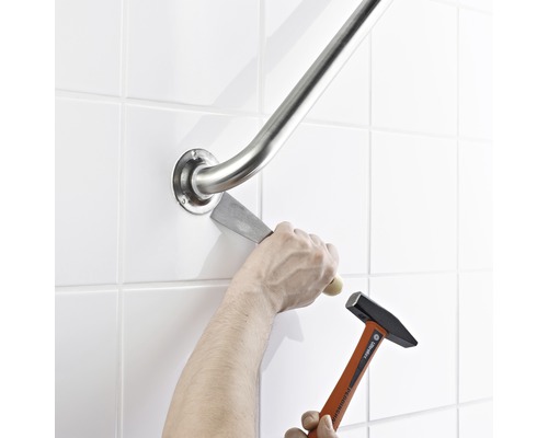 Eine Person entfernt eine Haltestange mit Hammer und Meißel von der Wand.