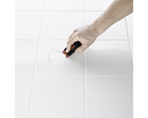 Hand mit Fugenkratzer entfernt Fugenmasse zwischen Platten.
