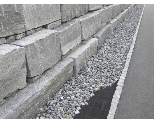 Eine Stützmauer aus grauen Granitblöcken mit Kiesbett.