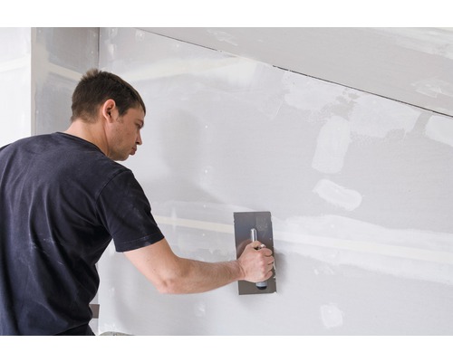 Un homme enduit un mur en plaques de plâtre avec une spatule