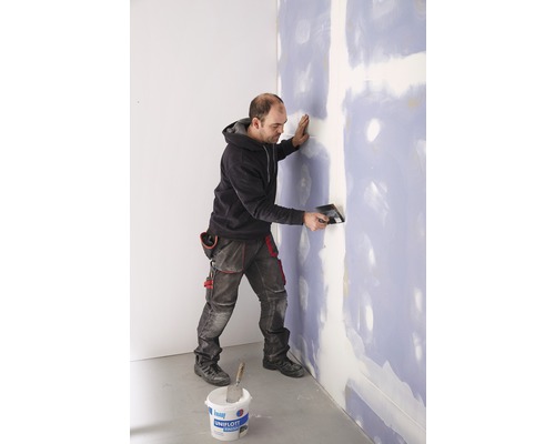 Un homme enduit un mur avec du mastic et une spatule