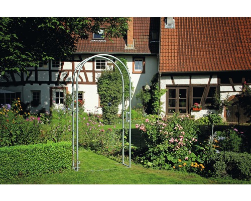 Gartenszene mit Rosenbogen aus Metall vor einem Fachwerkhaus