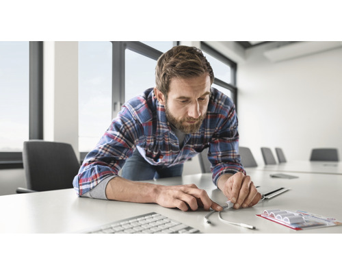 Un homme range des câbles avec des serre-câbles sur un bureau. Clavier, téléphone et salle de réunion en arrière-plan.