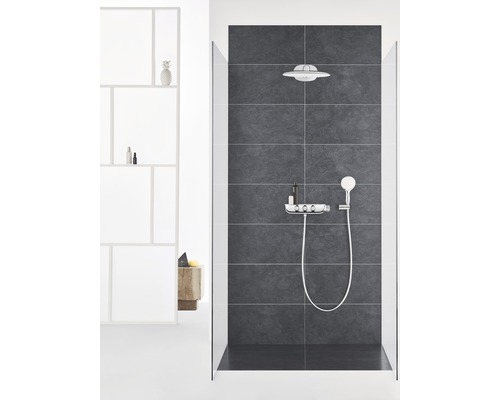 Douche moderne avec pomme de tête, douchette à main et étagère sur fond de carrelage foncé.