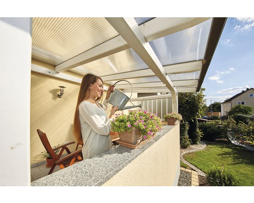 Eine Frau giesst Blumen auf einem Balkon mit transparentem Dach.