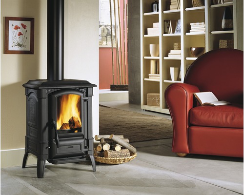 Poêle en fonte avec bois brûlant dans un salon avec fauteuil et bibliothèque