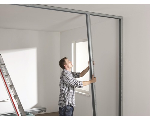 Un homme installe une cloison sèche avec des profilés métalliques dans une pièce.