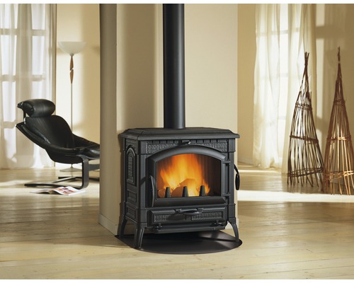 Poêle à bois noir avec feu de bois dans un salon avec des fauteuils et des décorations.