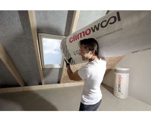 Ein Mann trägt eine Rolle Climowool Dämmwolle auf seiner Schulter in einem Dachgeschoss.