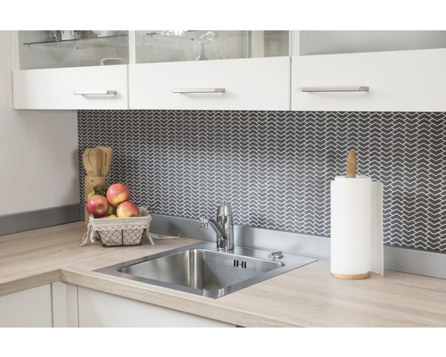 Évier de cuisine en acier inoxydable avec robinet et ustensiles de cuisine sur un plan de travail clair devant un fond sombre à motifs