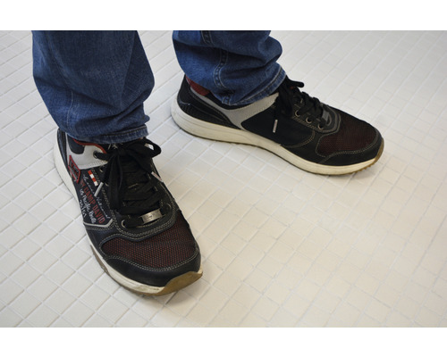 Une paire de chaussures à lacets en textile et matière synthétique au pied d''une personne.