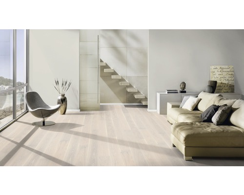 Salon lumineux avec parquet, canapé, fauteuil et escalier