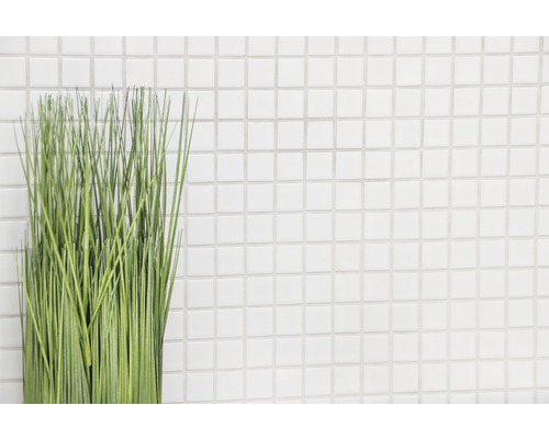 Plante artificielle décorative verte devant un mur avec des carreaux carrés blancs