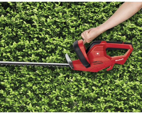 Einhandbedienung einer roten Einhell Heckenschere vor einer grünen Hecke.