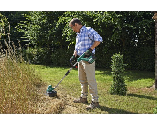 Mann schneidet Gras mit einem Akku-Rasentrimmer im Garten.