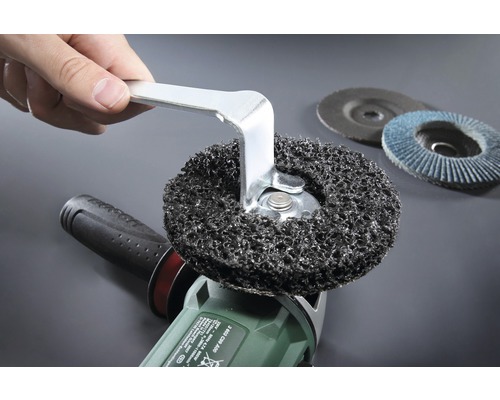 Main changeant un disque abrasif sur une meuleuse d''angle avec une clé à fourche