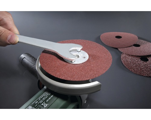 Un disque abrasif est fixé à une meuleuse d''angle avec une clé.