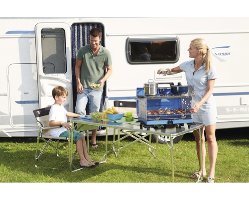 Famille en camping avec caravane, table de camping, chaise de camping et réchaud à gaz